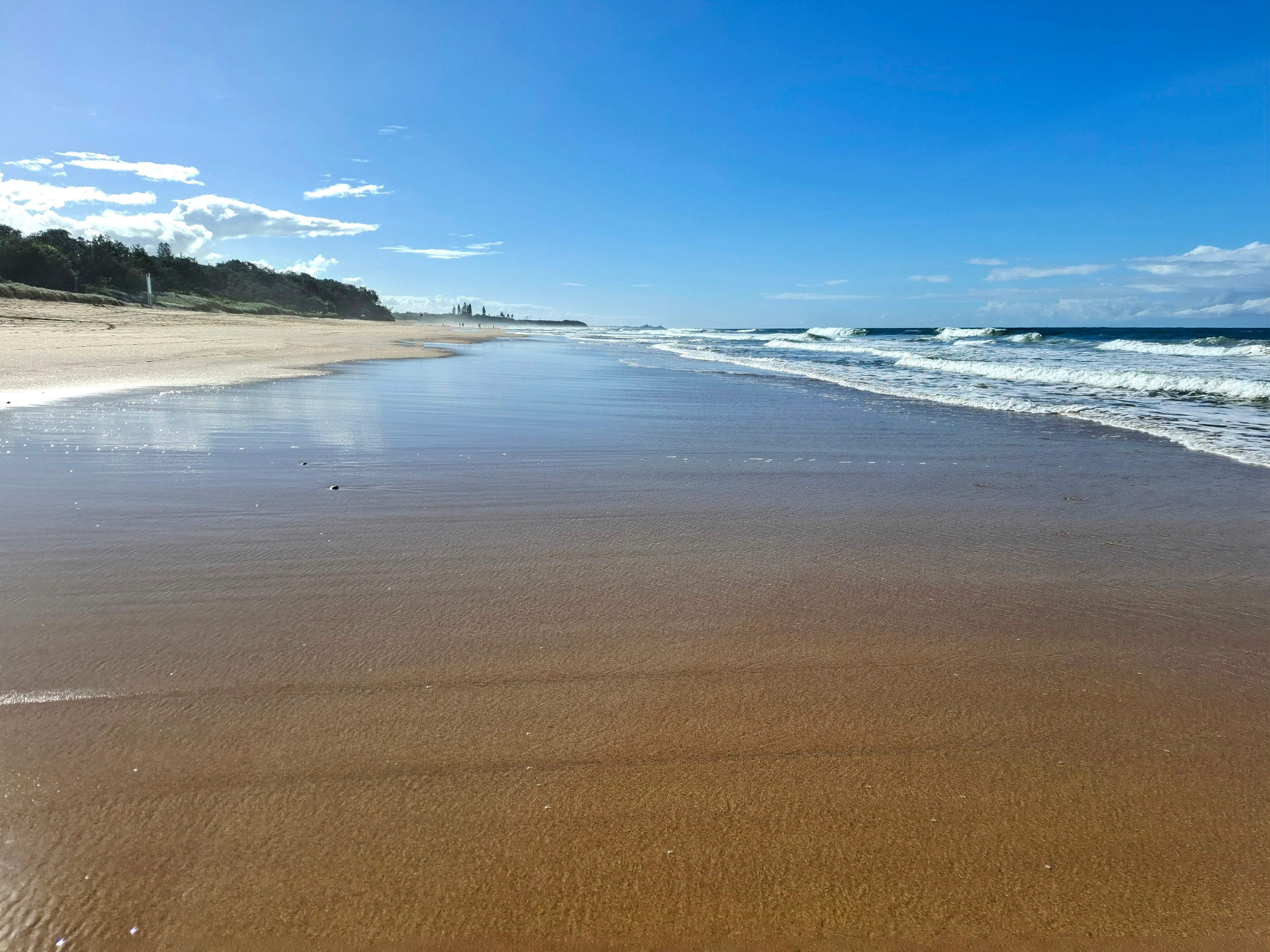 Flat sand and a calm beach water on right, blue sky day Flat sand and a calm beach water on right, blue sky day