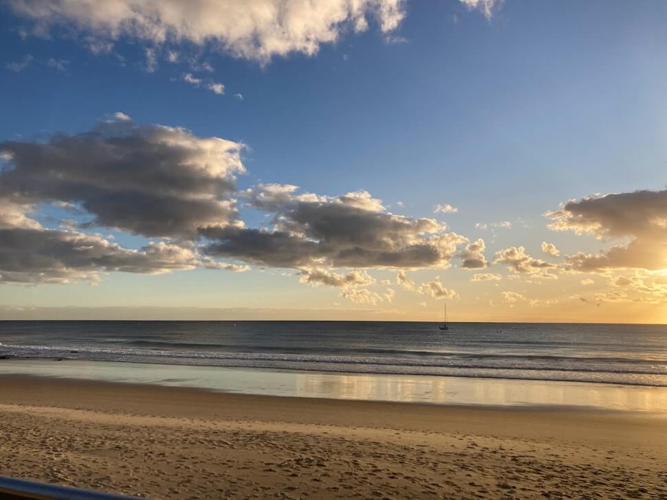 Sunrise on Mooloolaba beach, Australia. Golden sand, puffy white clouds and a sail boat in the distance