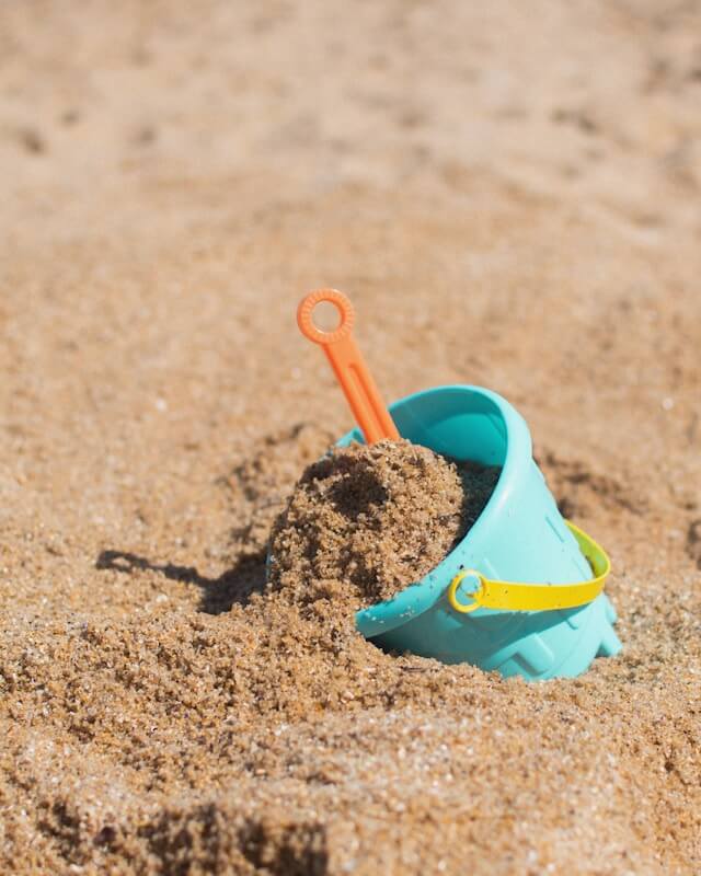 blue bucket and orange handle of a spade sticking out of the sand