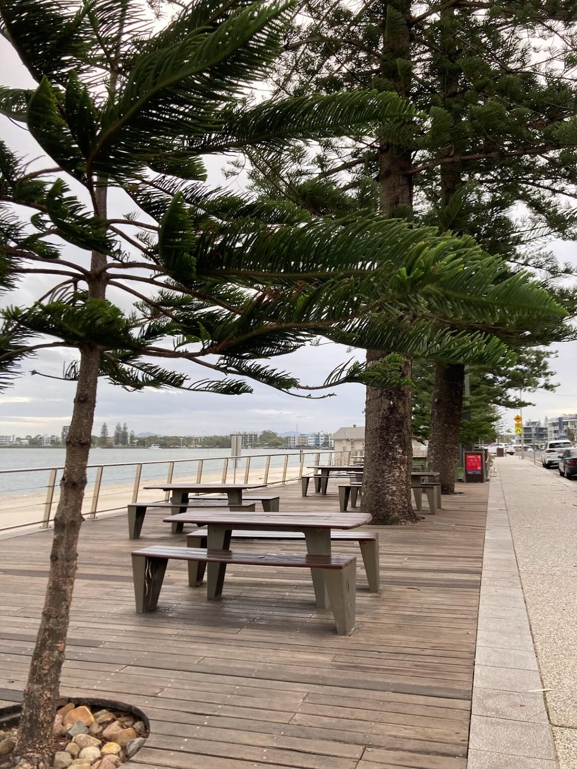 picnic tables and trees on boardwalk. Coral sea to left