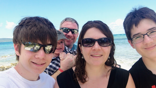 Family of 5 take a selfie on the beach. Water in background. Three boys a mum and a dad