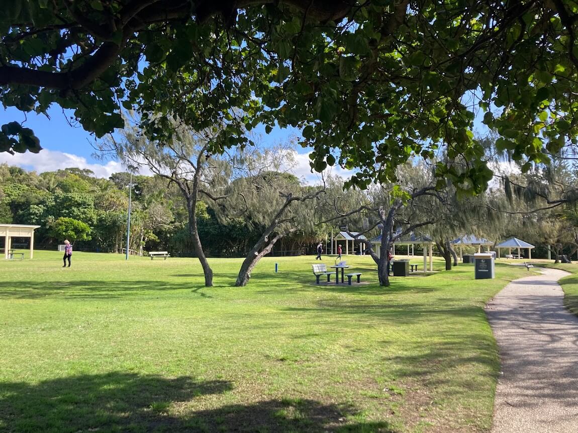 greenspace with trees and a paved footpath. Covered BBQ area in background