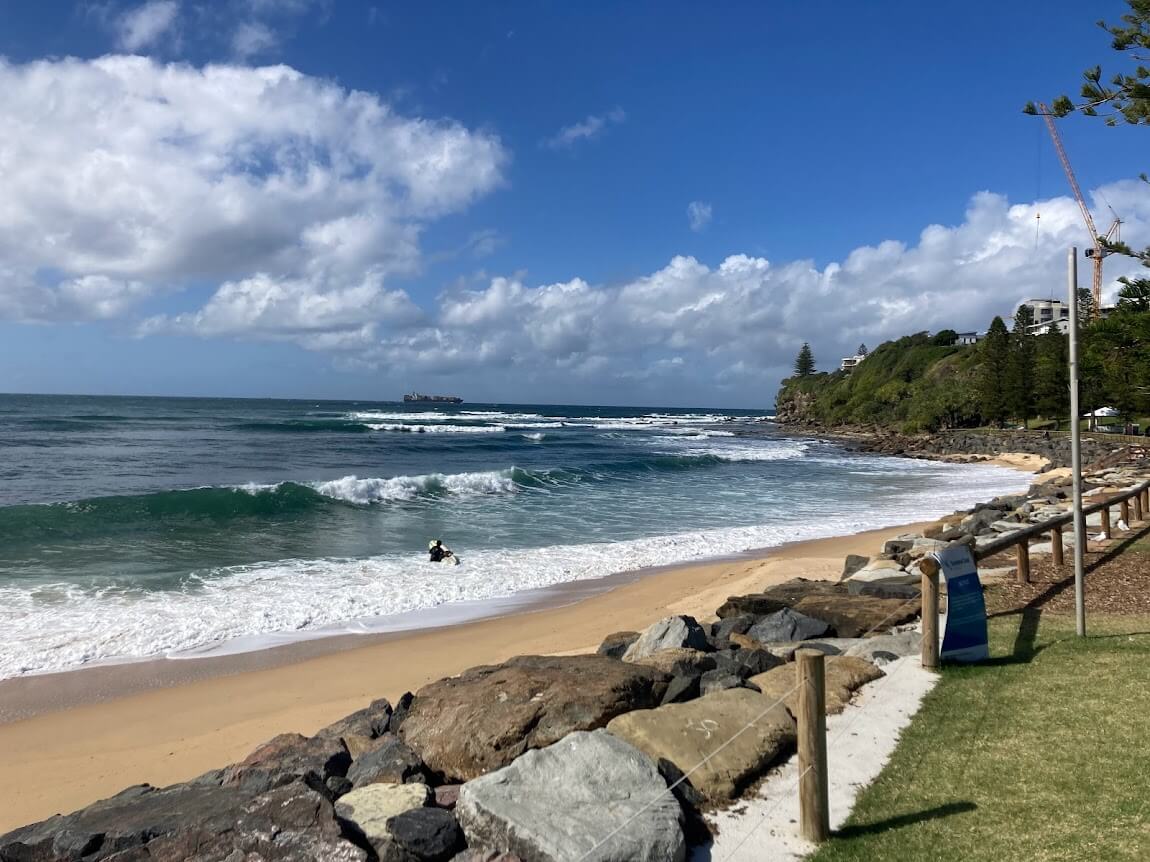 Surfer heading out in ocean with a cargo ship far in distance